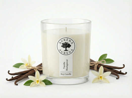 „Auréna Duftkerze Vanilla Madagascar im klaren Glas mit weißem Wachs, arrangiert mit Vanilleschoten und Vanilleblüten vor hellem, neutralem Hintergrund.“