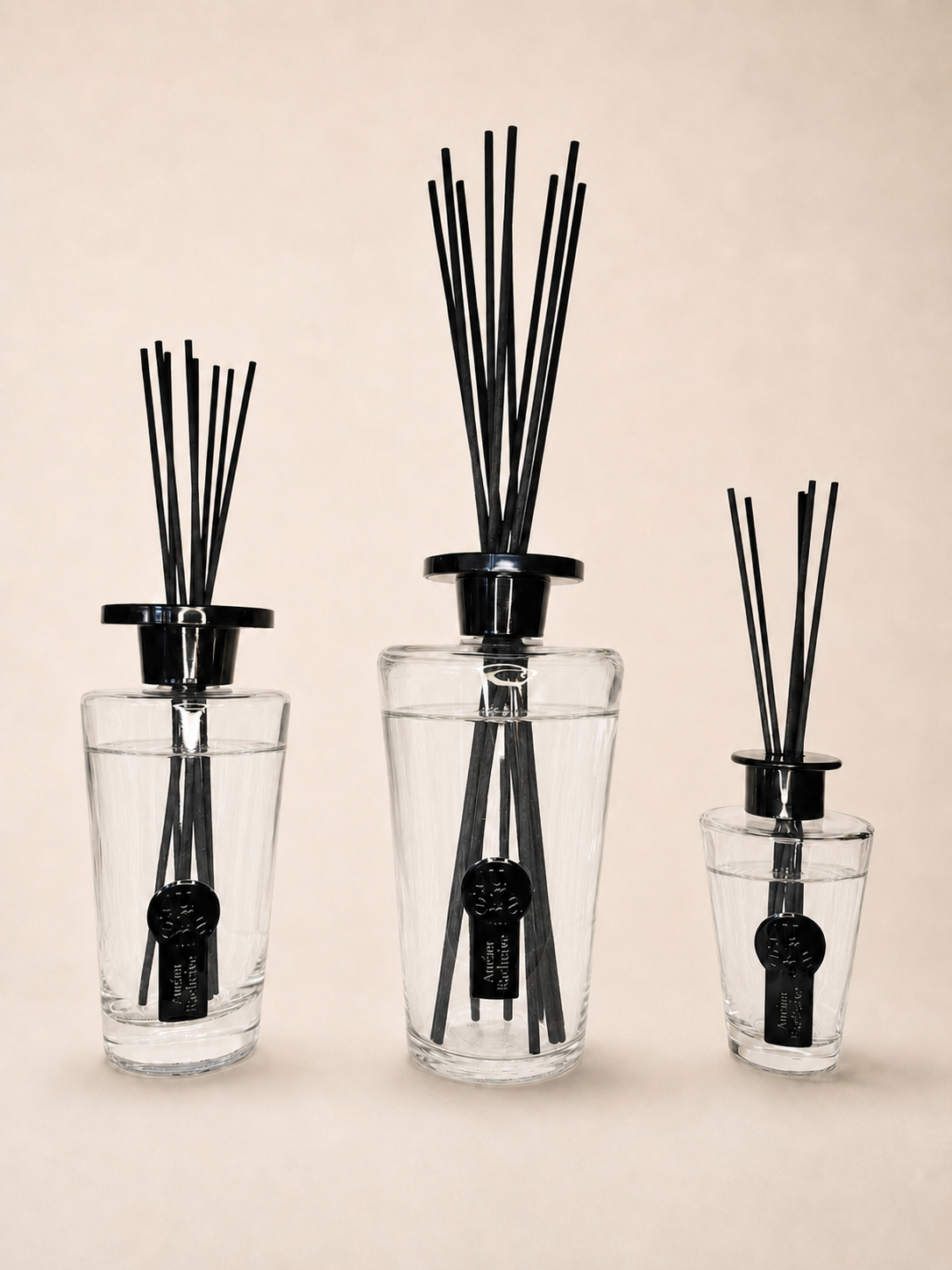 Drei Auréna Raumduft-Diffuser aus klarem Glas, der 1.000-ml-Diffuser mittig, vor cremefarbenem Hintergrund.
